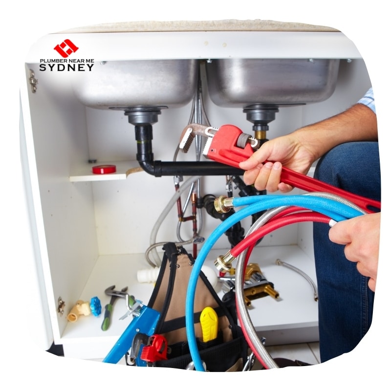 Plumber fixing a clogged kitchen sink with a wrench and hose.